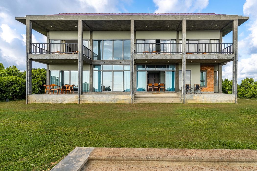 Modern concrete villa with floor-to-ceiling windows, balconies, and surrounding lawn.