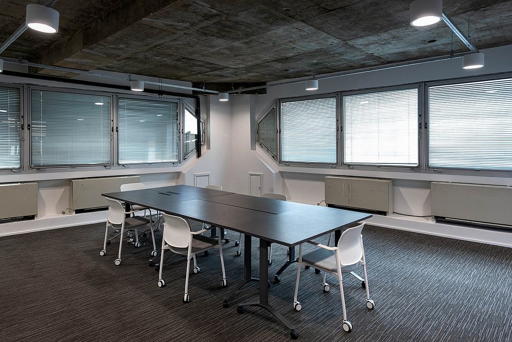 A modern, minimalist office space with a concrete ceiling, large windows, and sleek furniture.