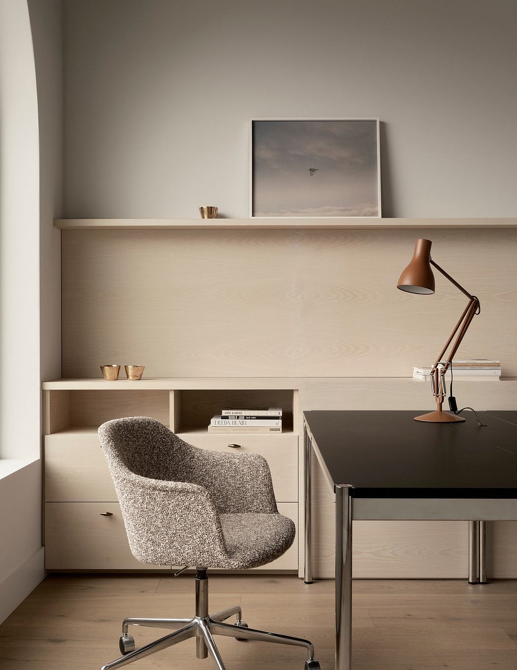 Modern, minimalist home office with neutral-toned shelving, desk, and textured swivel chair.