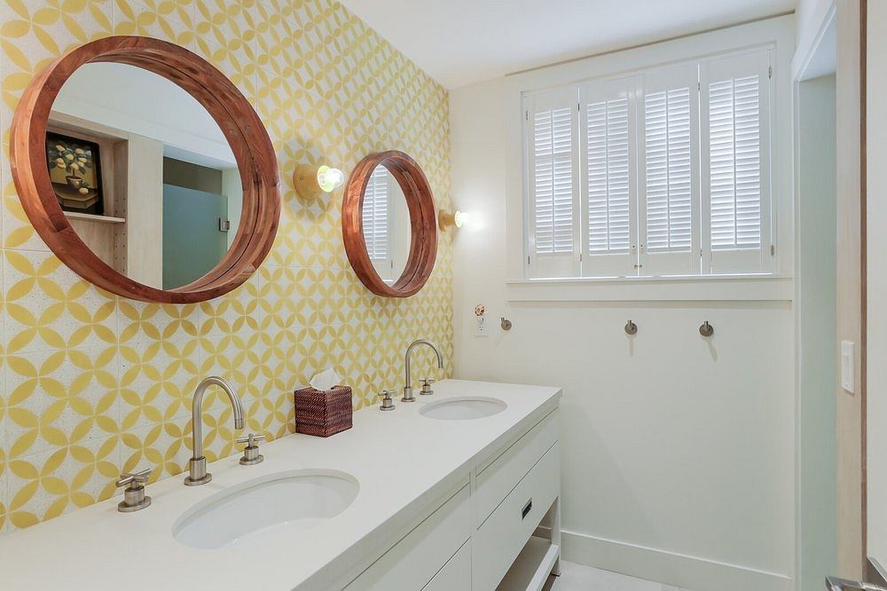 Vibrant yellow wallpaper, round wooden mirrors, and a sleek white vanity in this bathroom.