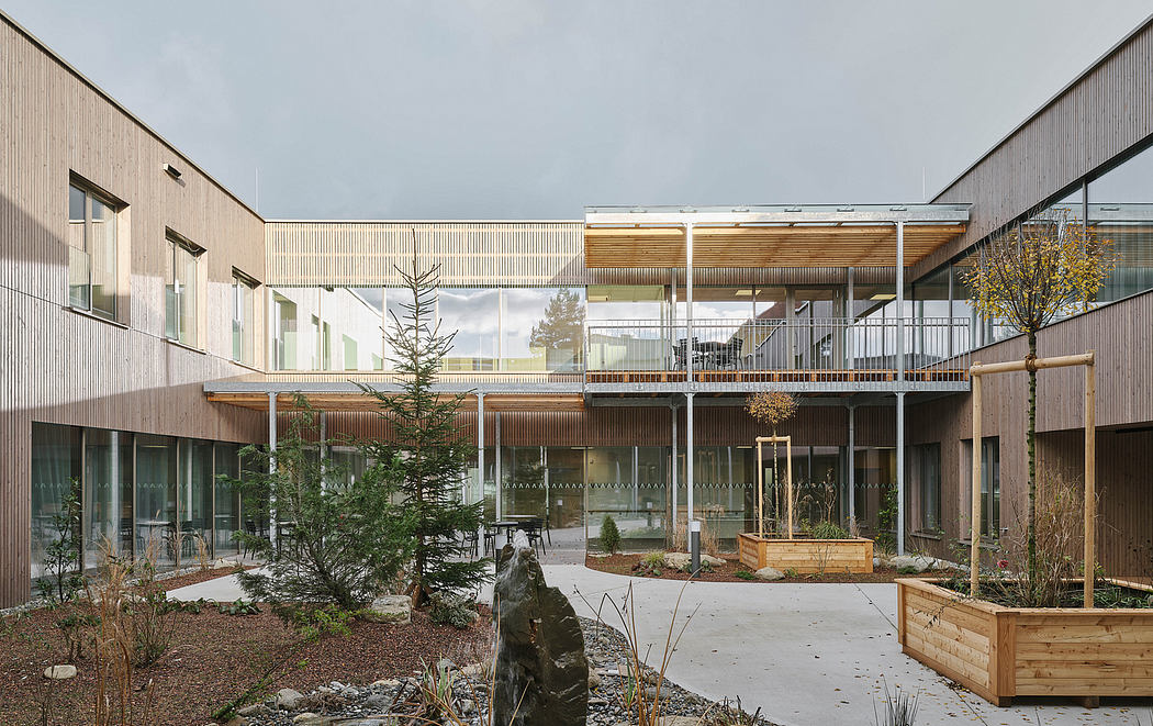 Modern wooden building with glass walls, balconies, and landscaped courtyard.