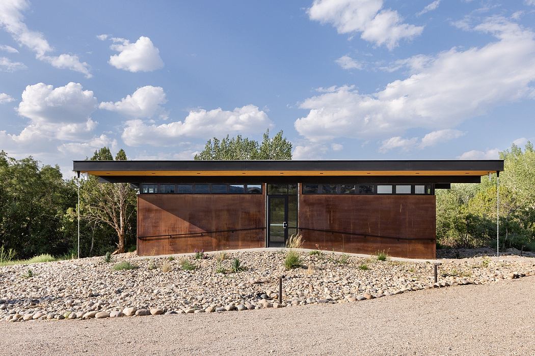 A modern, single-story structure with a flat roof, wood siding, and large windows overlooking a natural landscape.