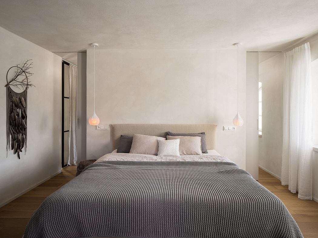 Minimalist bedroom with pendant lighting, plush bedding, and a modern wall hanging.