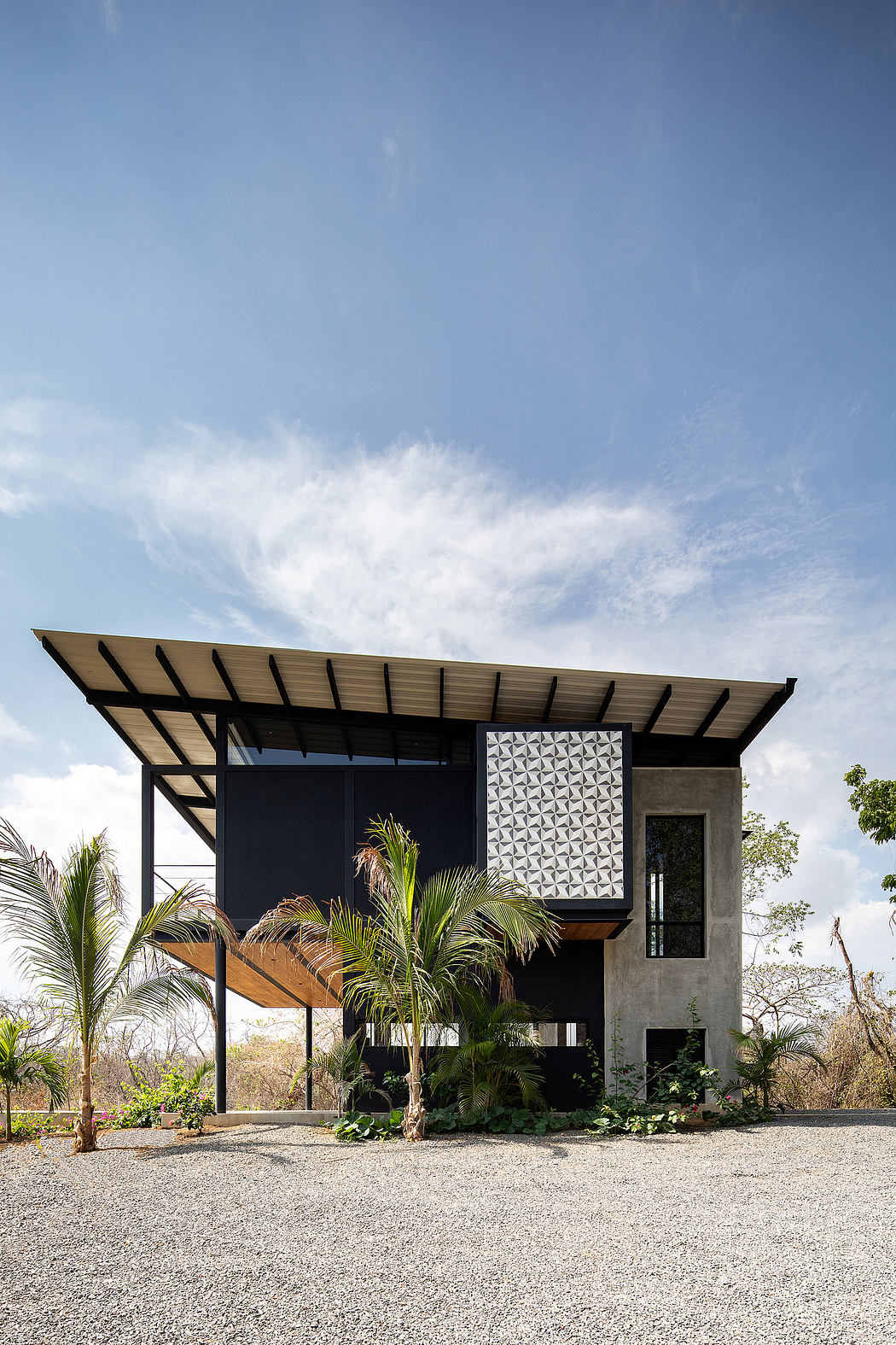 Modern tropical-inspired home with geometric facade, covered balcony, and lush vegetation.