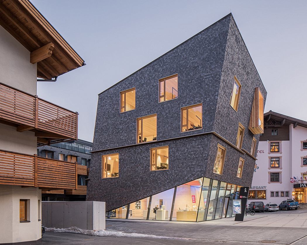 A modern building with a slanted slate roof and large glass windows, set in a winter landscape.