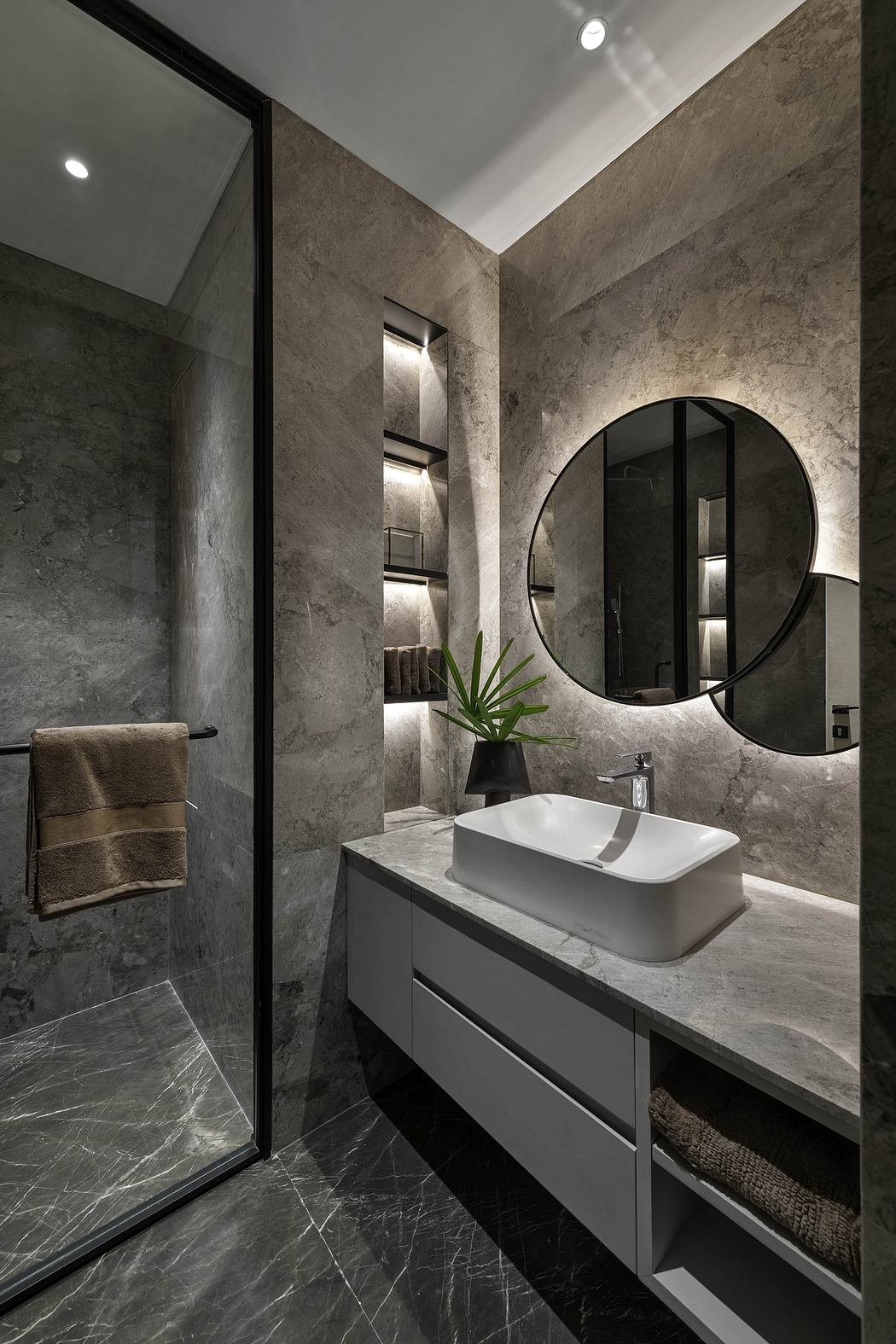 Modern bathroom with sleek marble walls, round backlit mirror, and floating vanity.