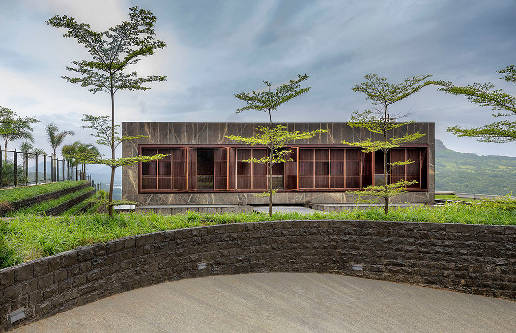 A modern, wooden-framed building with large windows amid lush greenery and a scenic backdrop.