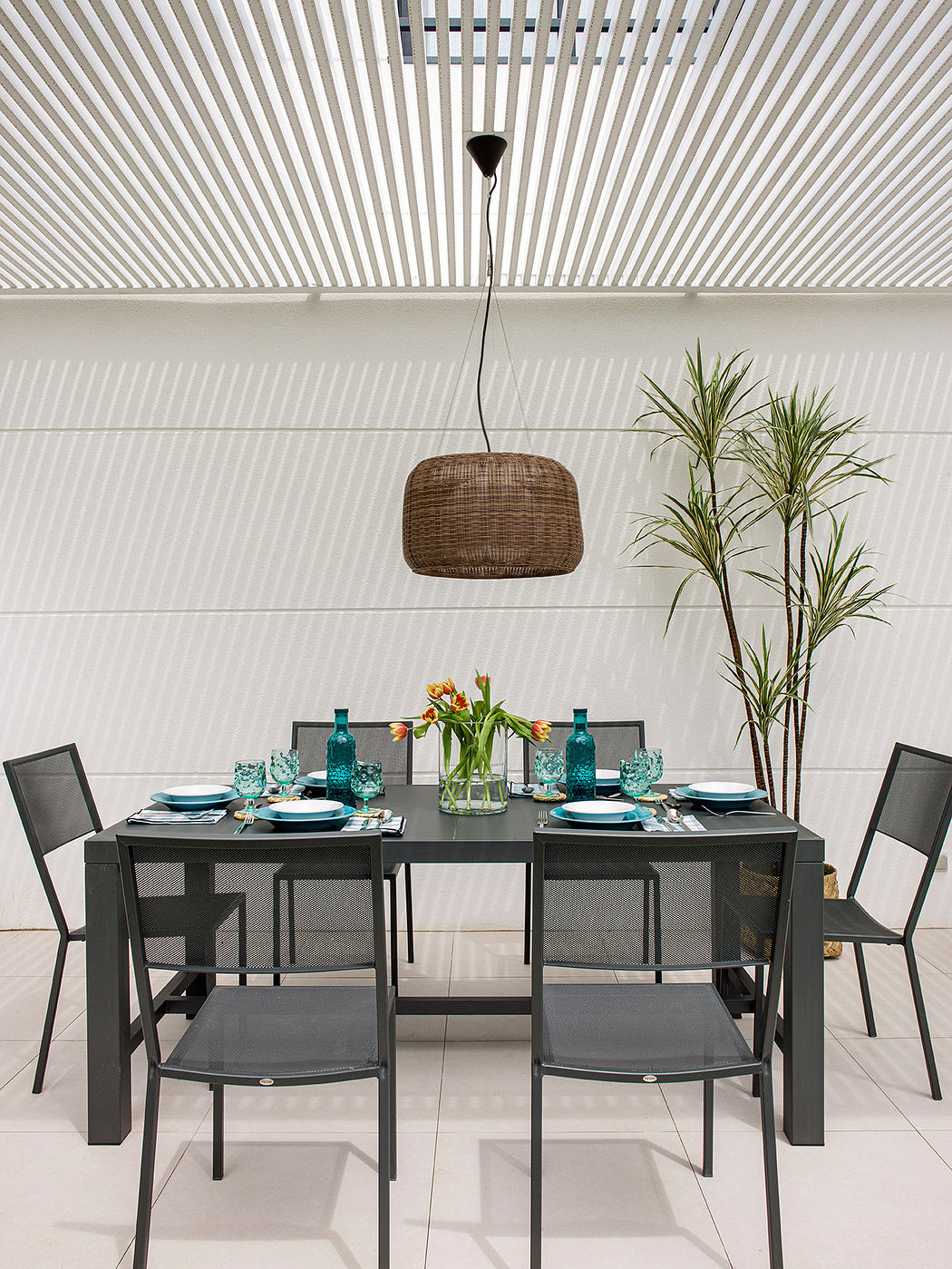 A modern dining room with a wicker pendant light, black furniture, and teal accents.