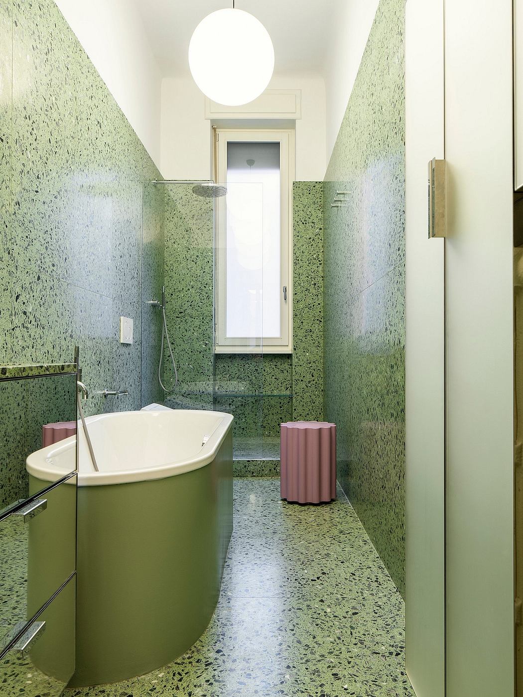 Minimalist bathroom with striking green terrazzo walls, circular mirror, and white bathtub.