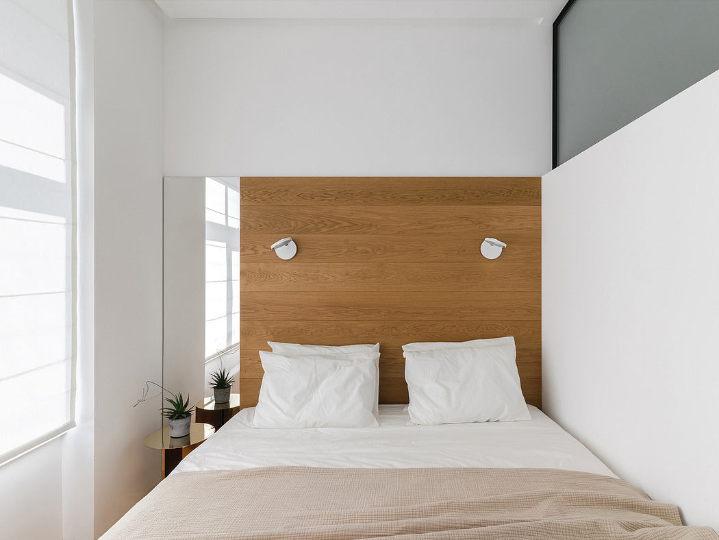 Minimalist bedroom with wooden headboard, neutral colors, and modern lighting fixtures.