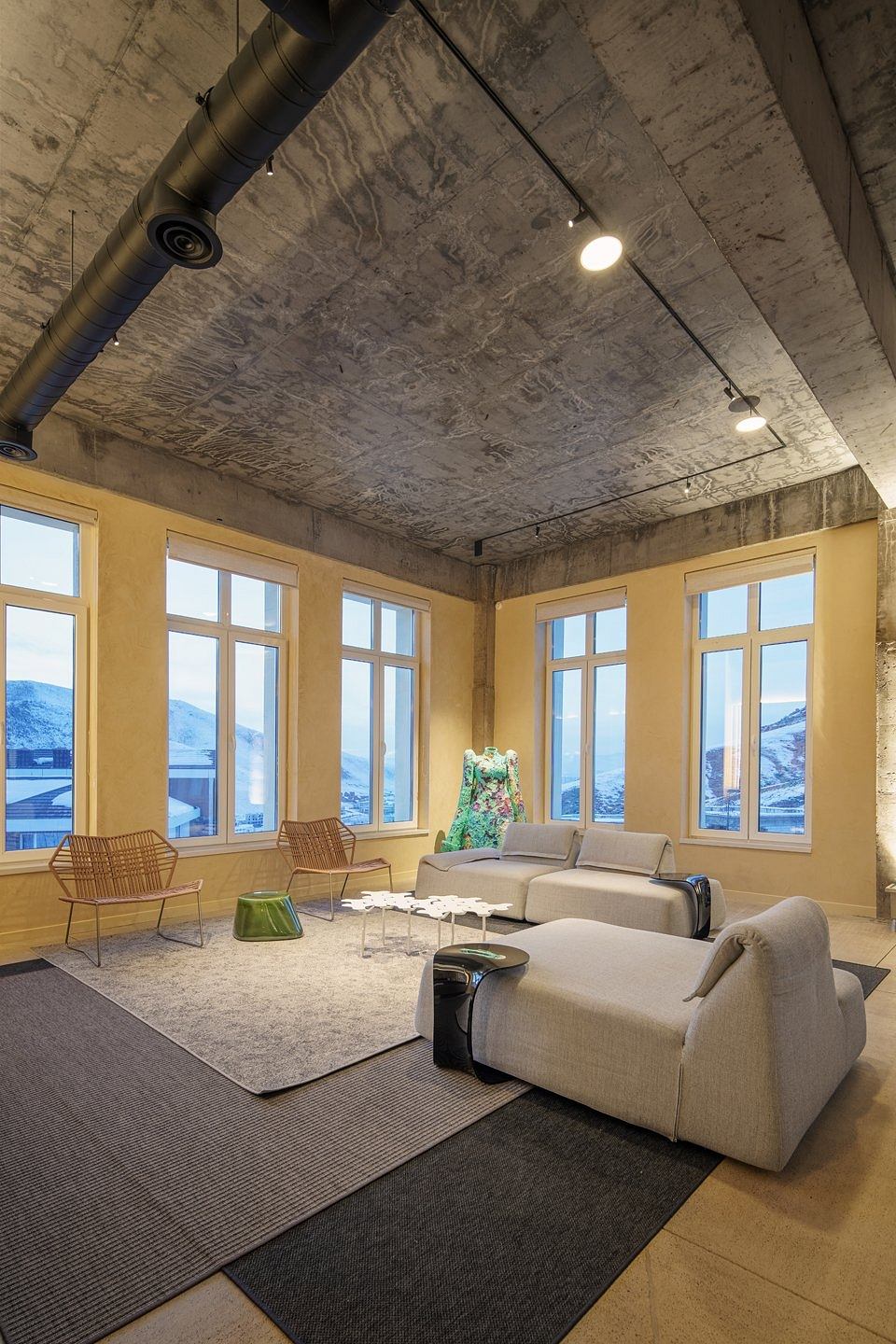 A modern and inviting living space with large windows, concrete ceiling, and stylish furniture.