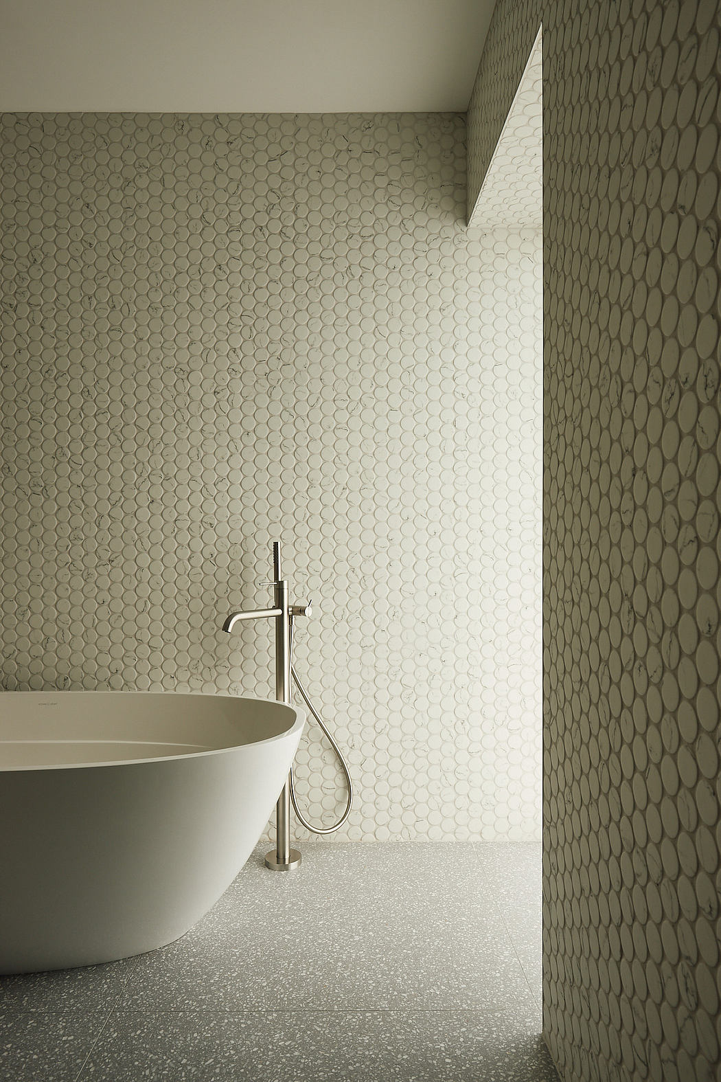 Minimalist bathroom with hexagonal tile wall, freestanding tub, and chrome faucet.