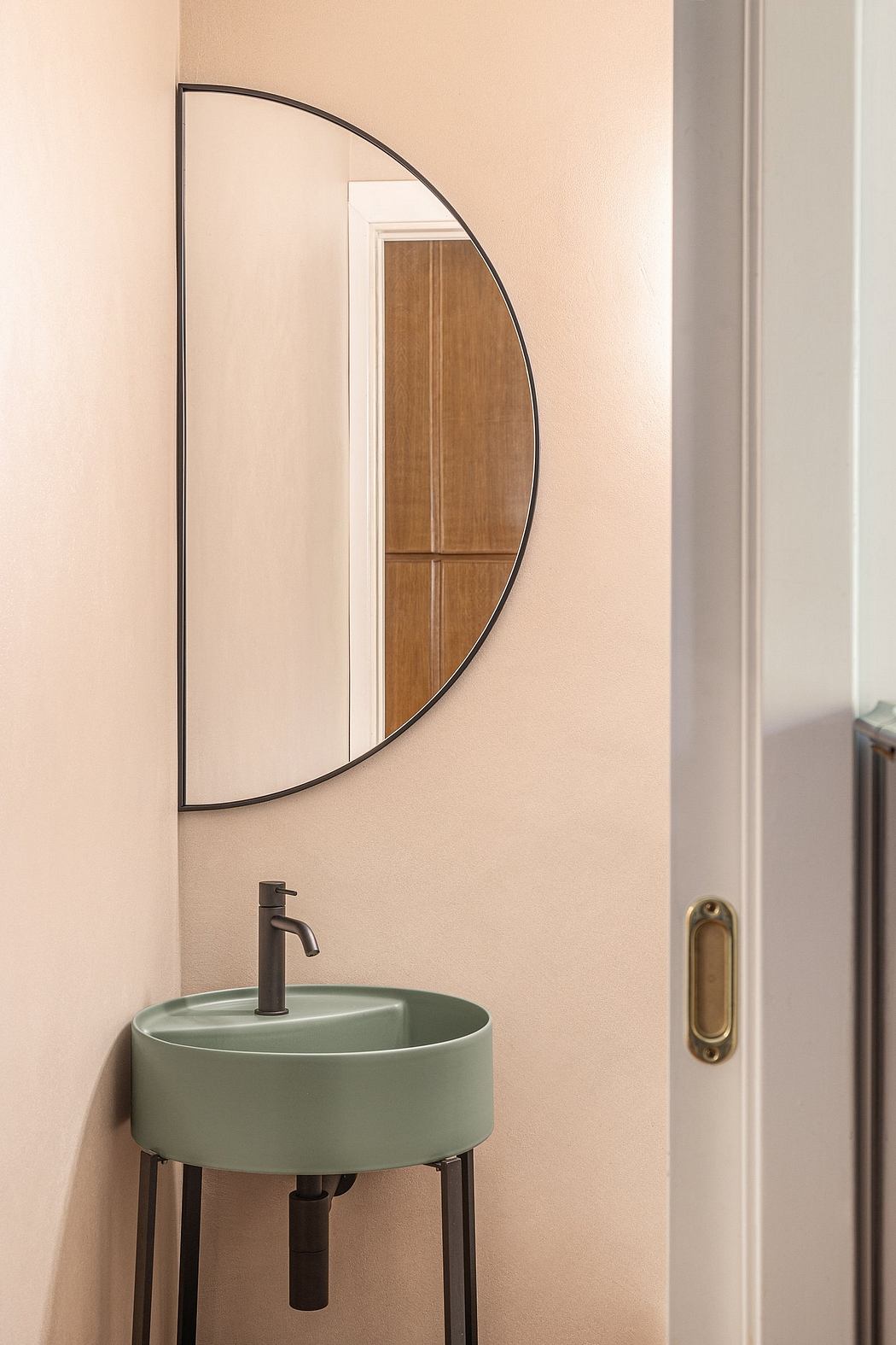 A modern bathroom with a curved oval mirror, a minimalist sink, and a brass door pull.