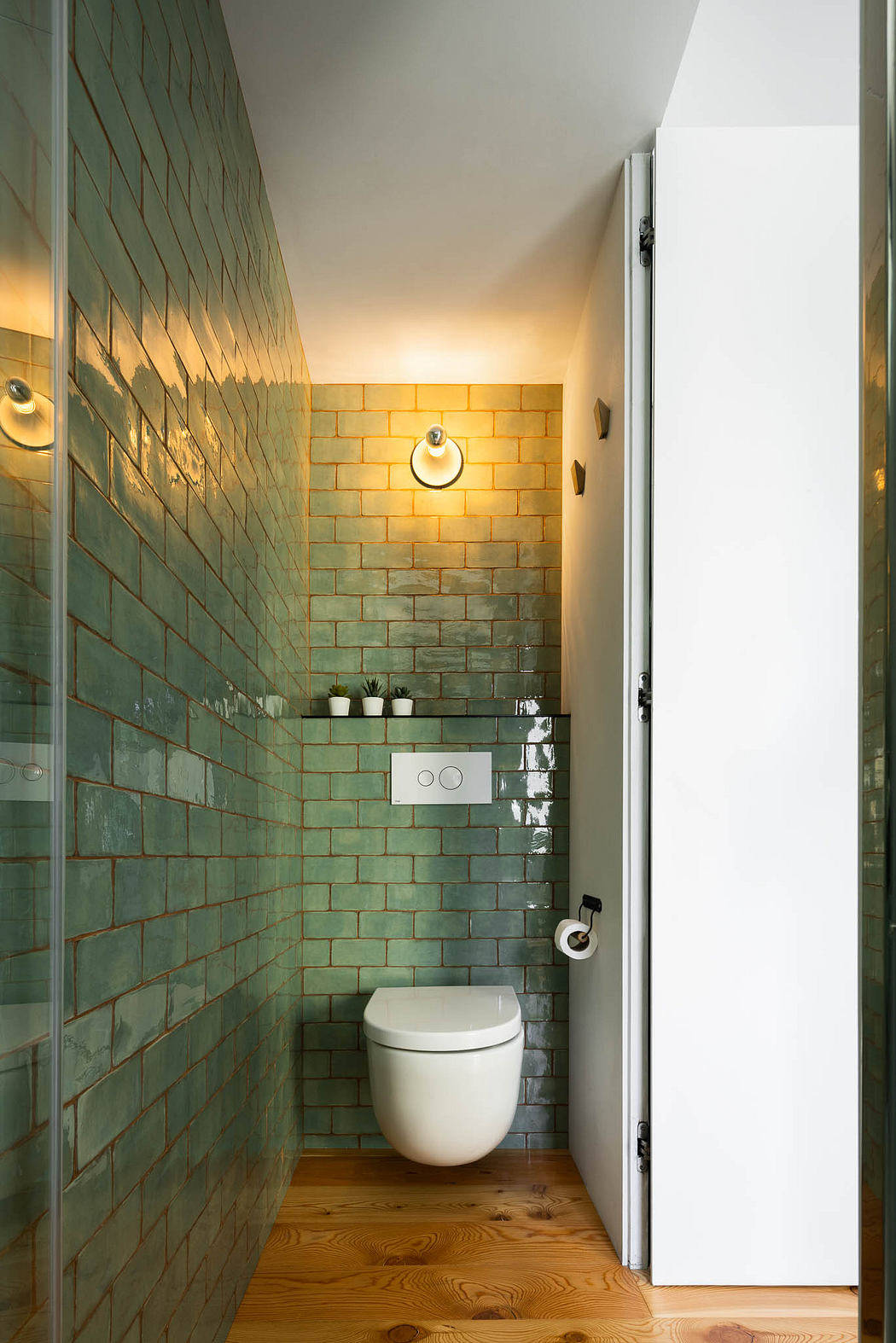 Compact bathroom with eye-catching green tile walls and modern wooden flooring.