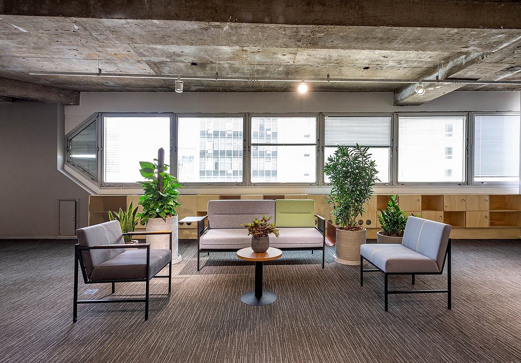 Modern industrial-style office lounge with wood-beamed ceiling, large windows, and greenery.