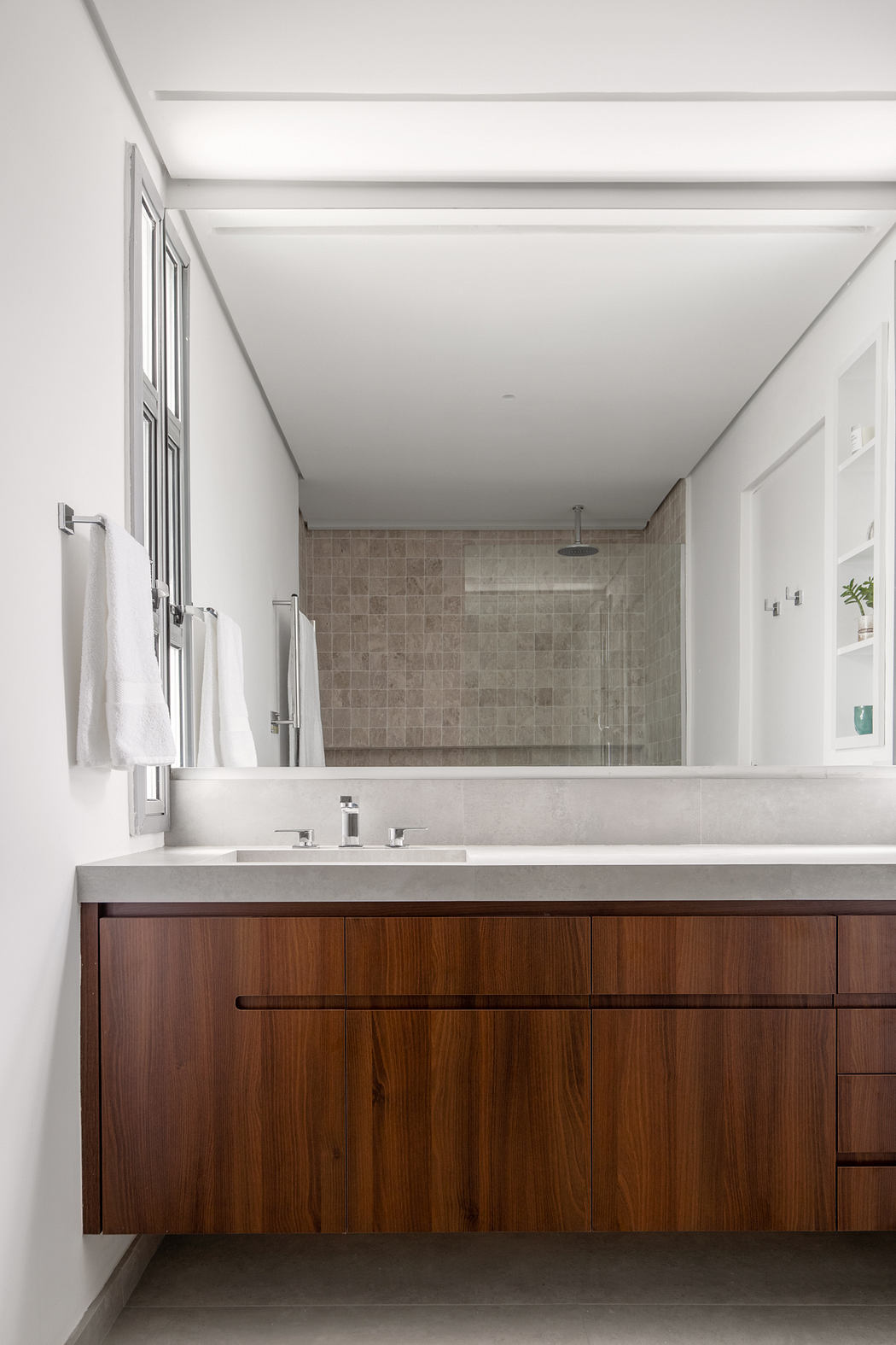 A modern bathroom with a wooden vanity, tiled wall, and frameless glass shower.
