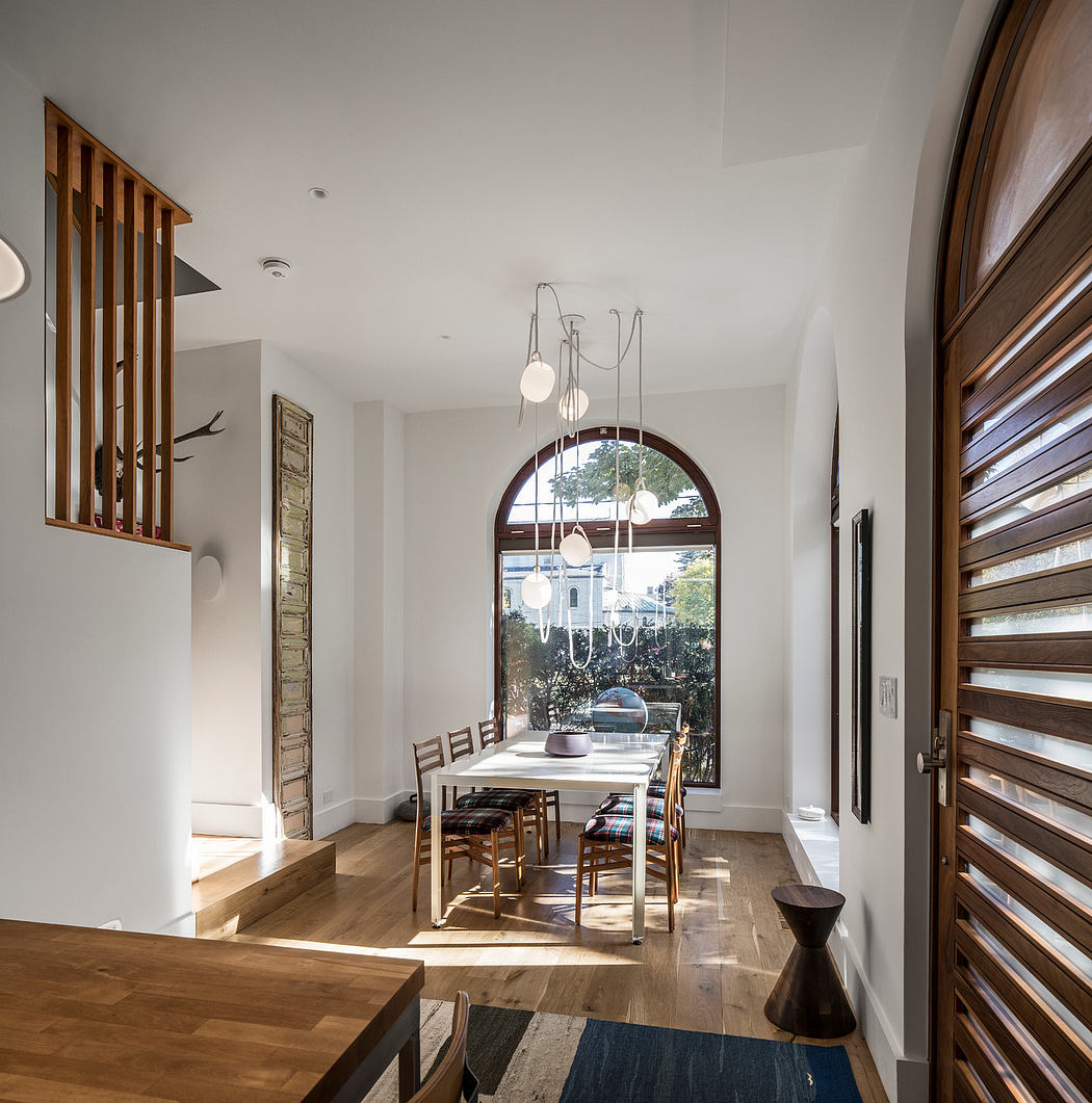 Modern dining room with arched window, wooden beams, and pendant lighting.