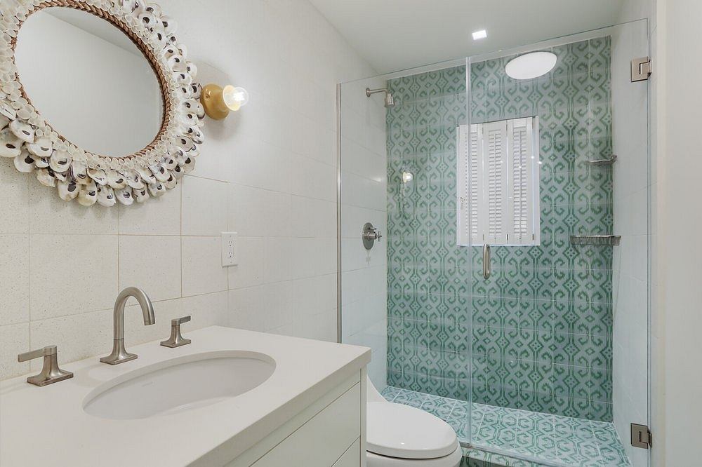 A modern bathroom with a patterned green tile wall, a round mirror, and a sleek vanity.