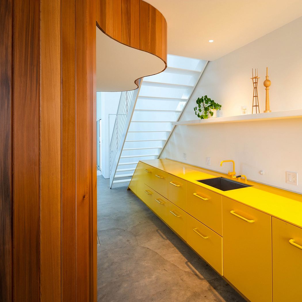 A modern kitchen with vibrant yellow cabinetry, curved wooden panels, and a sleek staircase.