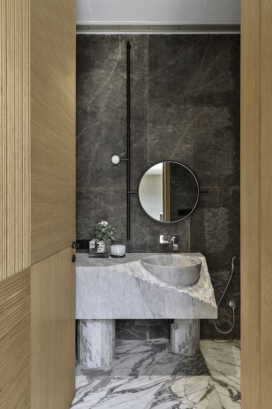Luxurious bathroom with dark marble walls, round mirror, and modern marble vanity.
