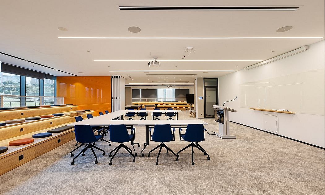 A modern lecture hall with tiered seating, sleek lighting, and vibrant orange accents.