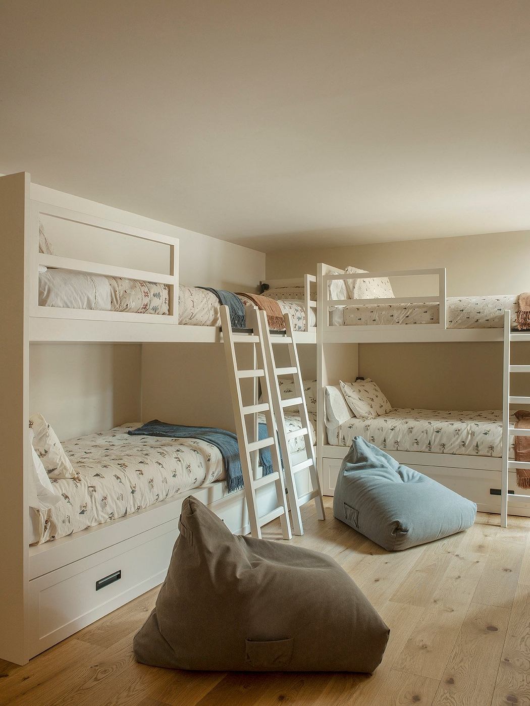 A cozy children's bedroom with bunk beds, bedding in natural tones, and beanbag chairs.