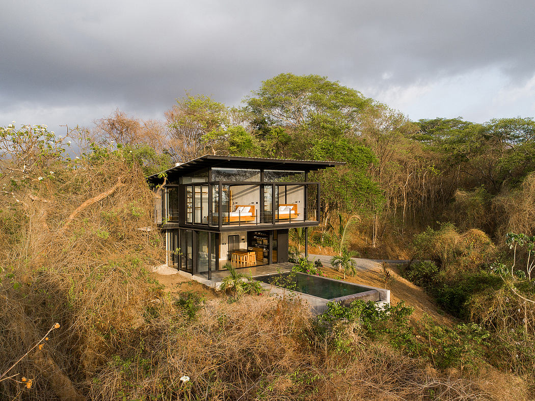 A modern, glass-walled house nestled in lush, tropical vegetation with a pool.