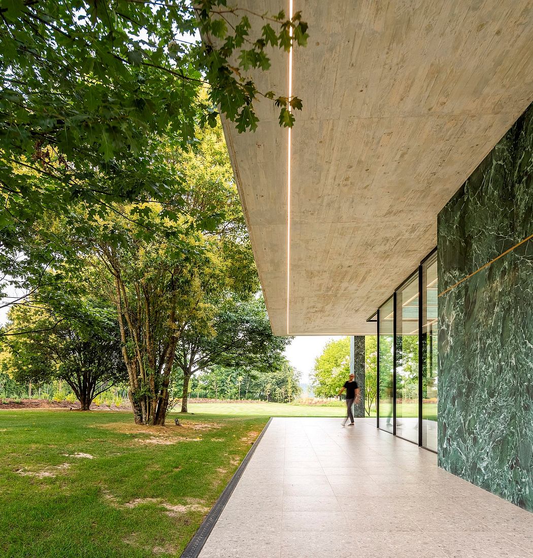 A modern glass-enclosed building flanked by a lush, green landscape and concrete walls.