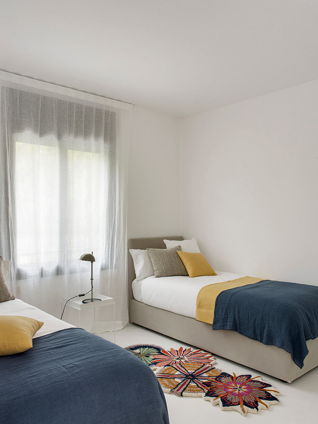 Minimalist bedroom with neutral palette, textured accents, and vibrant floral rug.