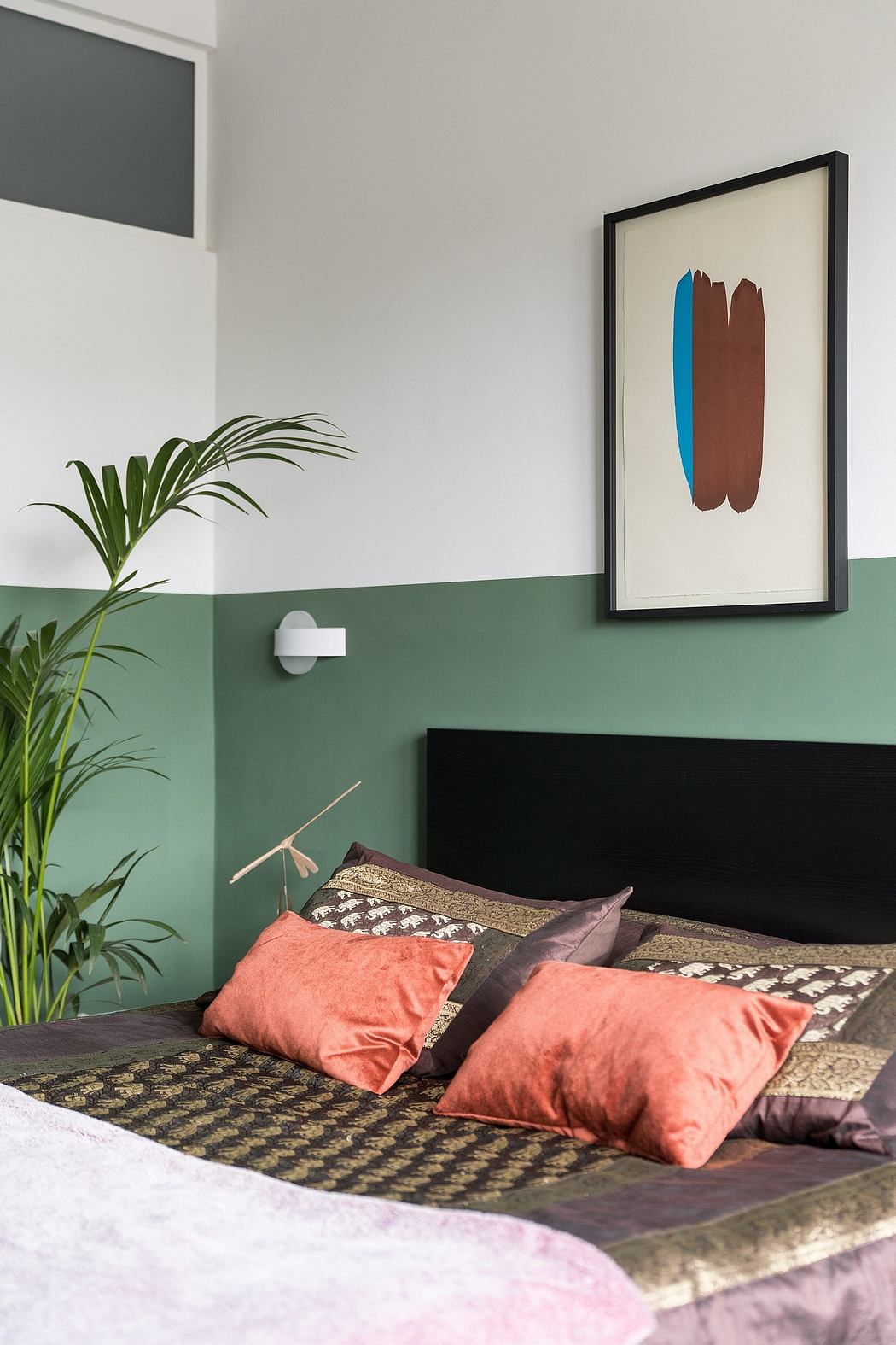 Modern bedroom with green accent wall, framed abstract art, and vibrant throw pillows.