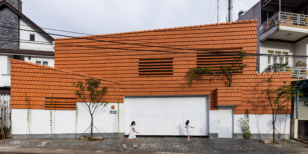 A modern brick building with distinctive angled roofing and two people walking on the pavement in front.