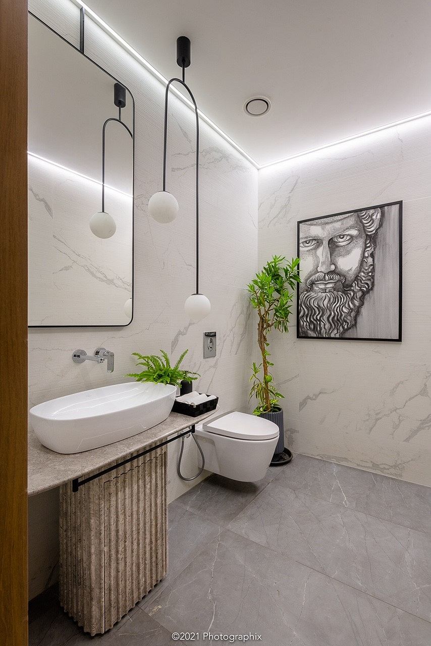 Modern bathroom with clean, minimalist design featuring marble walls, hanging pendant lights, and a framed portrait.