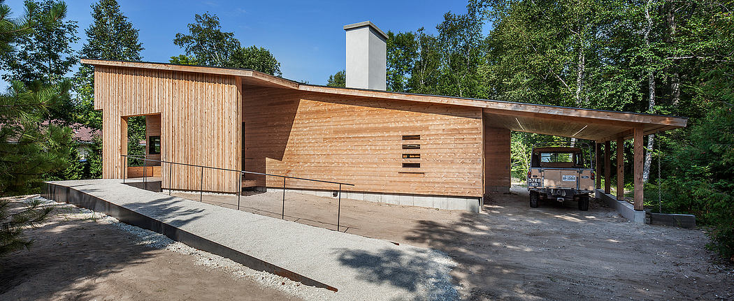 A modern wooden structure with a sloped roof and balcony, set amid lush greenery.