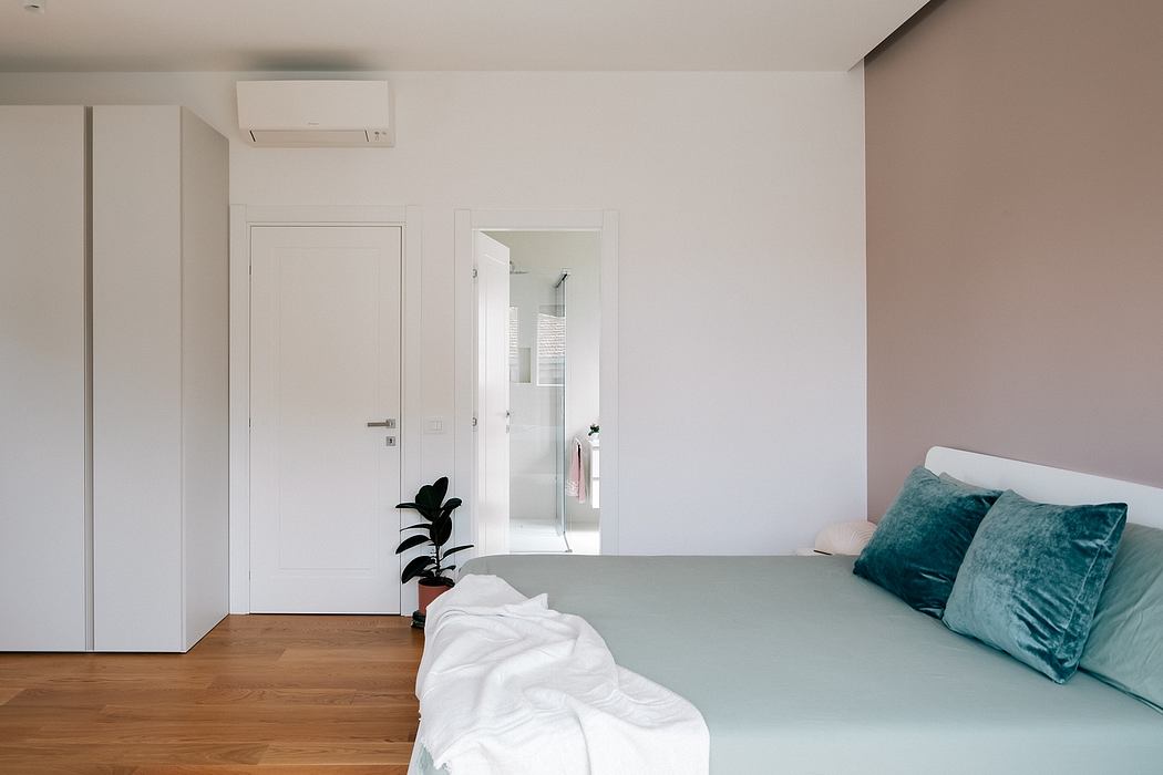 Minimalist bedroom with white walls, wooden floors, and green velvet throw pillows.