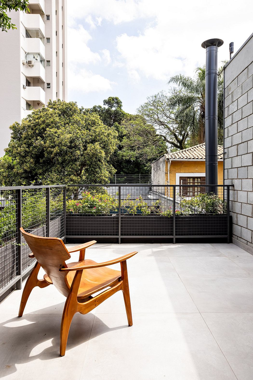 Sleek modern patio with wooden lounge chair, metal railing, and lush greenery backdrop.