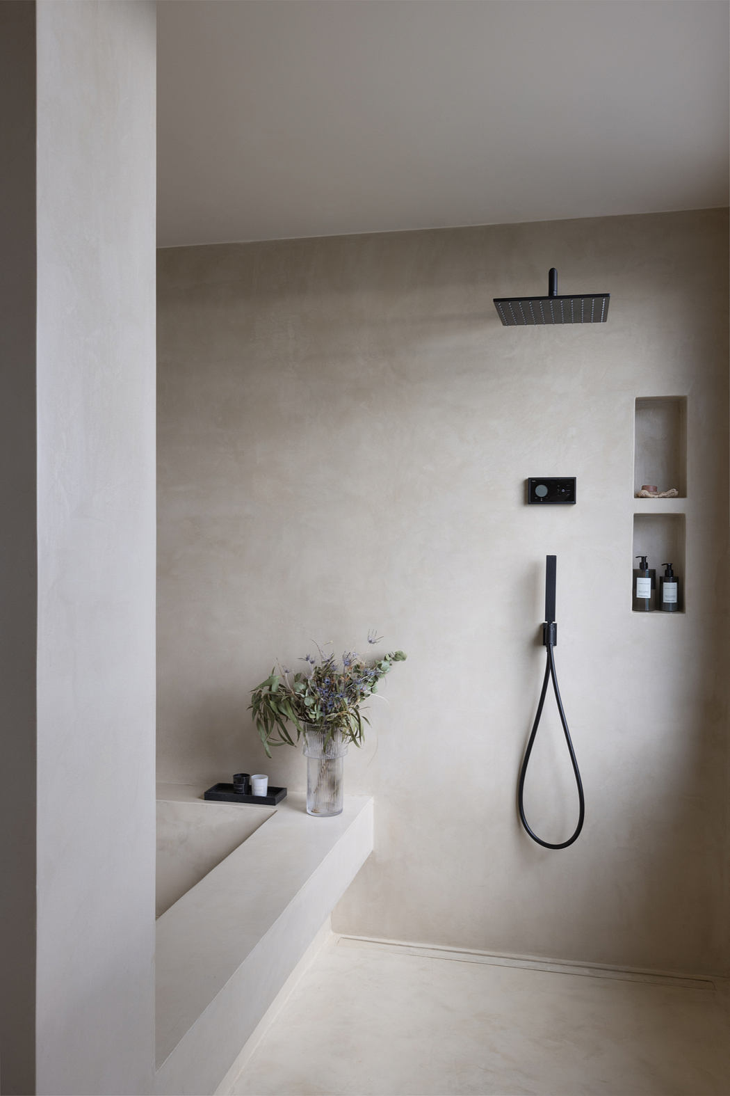 Minimalist bathroom design with sleek black fixtures, recessed shelving, and potted plants.