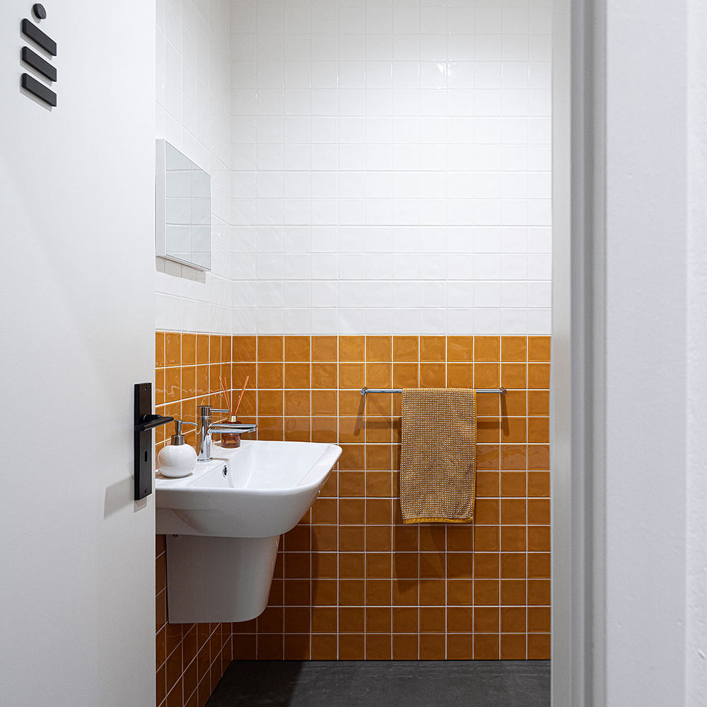 Minimalist bathroom interior with glossy orange tile walls, a white sink, and black accents.