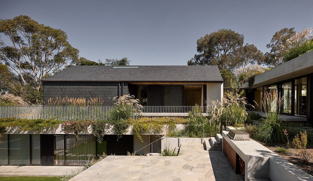 A modern, single-story home with a dark exterior, large windows, and a lush landscaped yard.