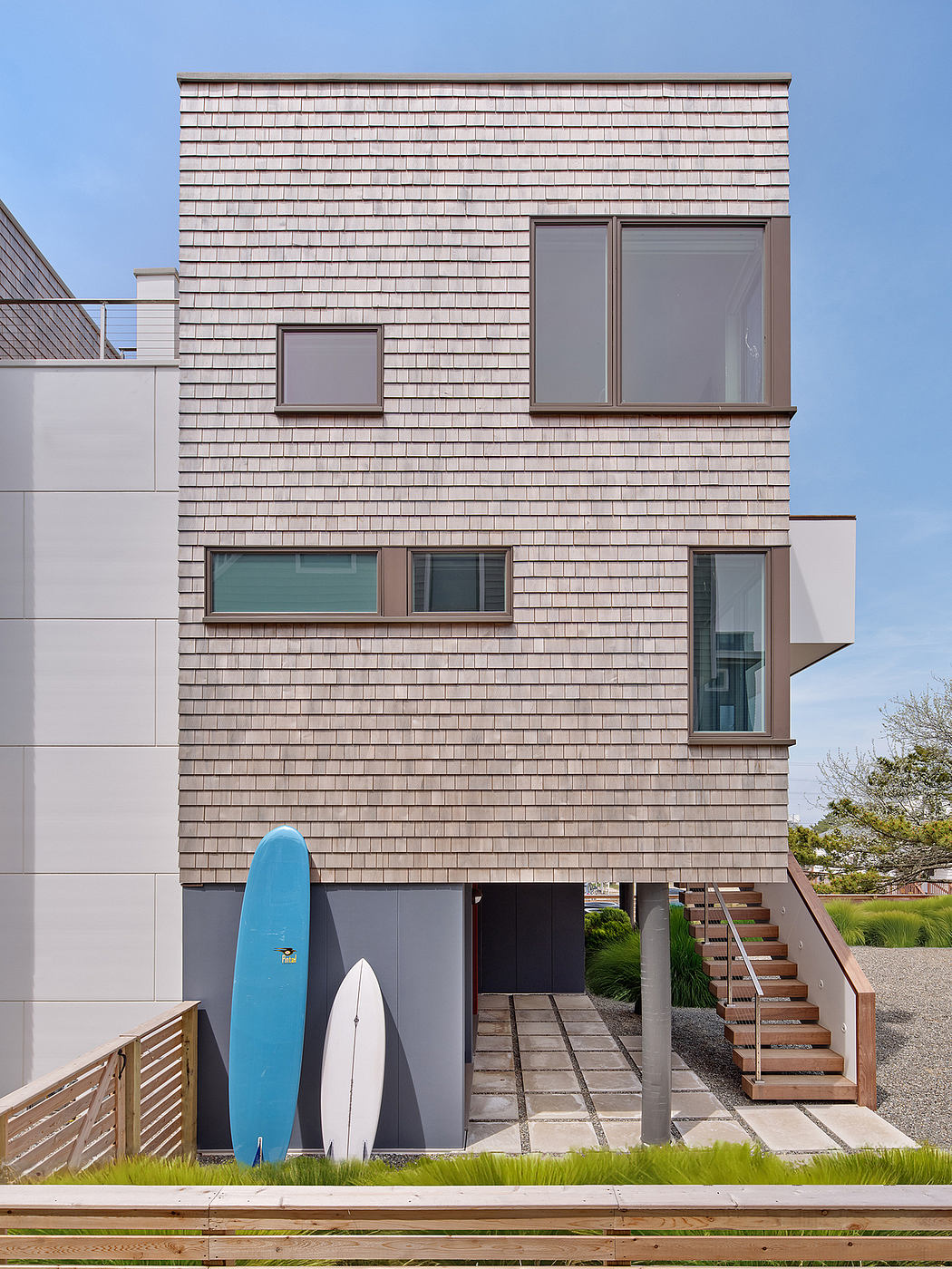 A modern two-story house with a wooden deck, surfboards, and a sleek exterior design.