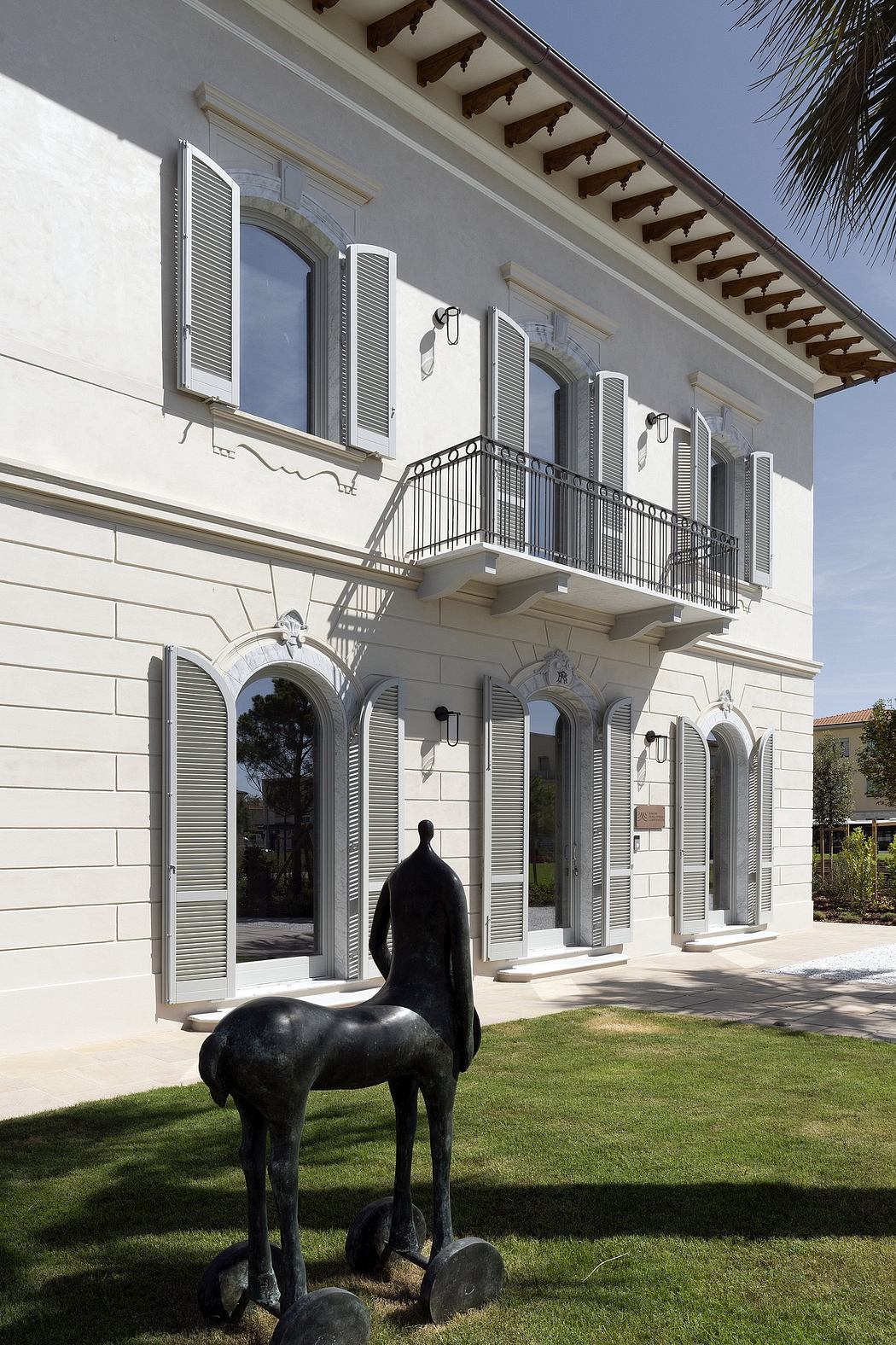 Elegant Mediterranean-style architecture with arched windows, louvered shutters, and a sculpture.