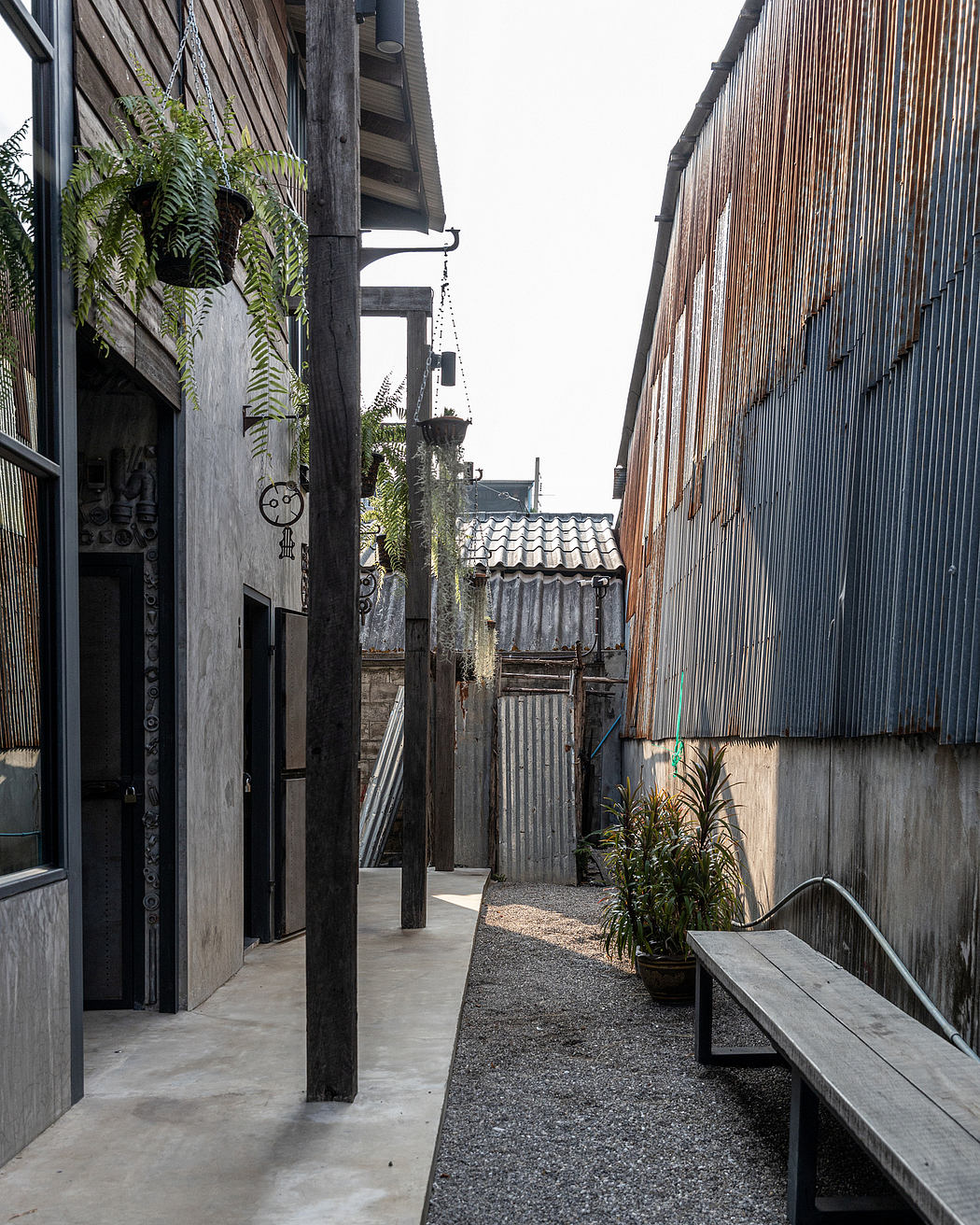 Narrow alley with rustic wooden structures, metal roofs, and potted plants, creating a serene atmosphere.
