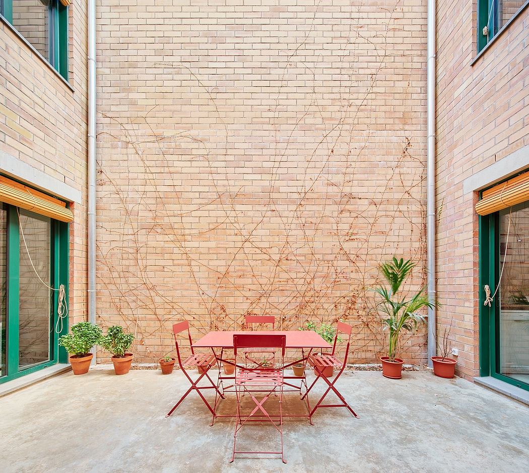 A cozy outdoor seating area with bright red bistro furniture and potted plants, framed by a cracked brick wall.
