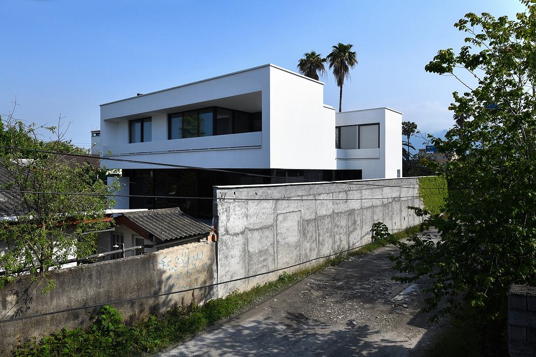 A modern, minimalist residential building with clean lines, large windows, and a stone retaining wall.