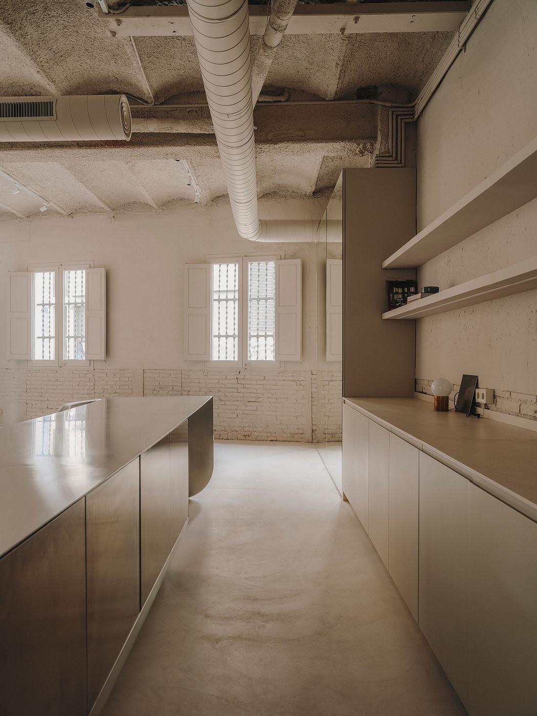 A spacious, modern kitchen with clean lines, white cabinets, and large windows, set against exposed brick walls.
