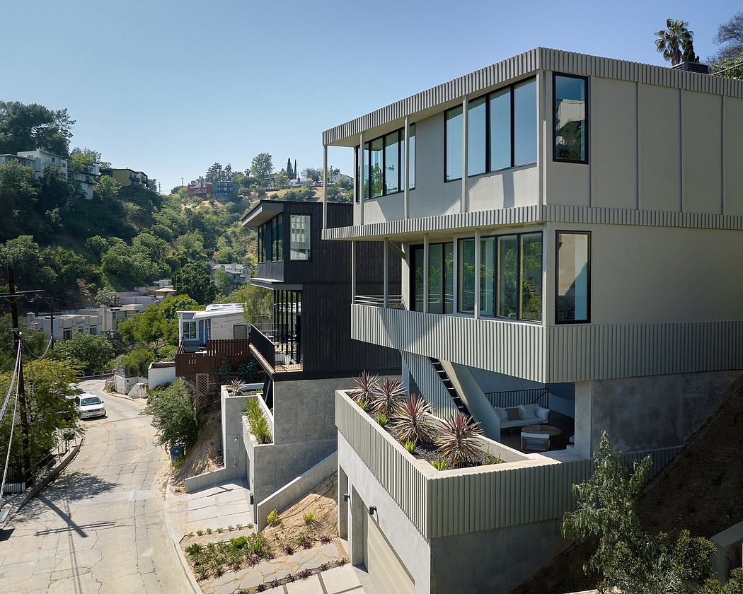 Modern, multi-level residence with sleek, minimalist gray exterior and large windows overlooking lush vegetation.