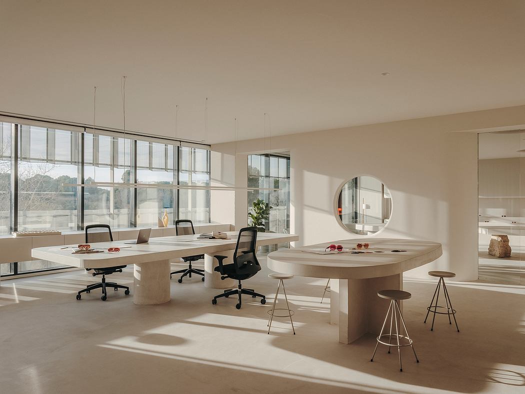Spacious modern office with sleek desks, circular table, and large windows providing ample natural light.