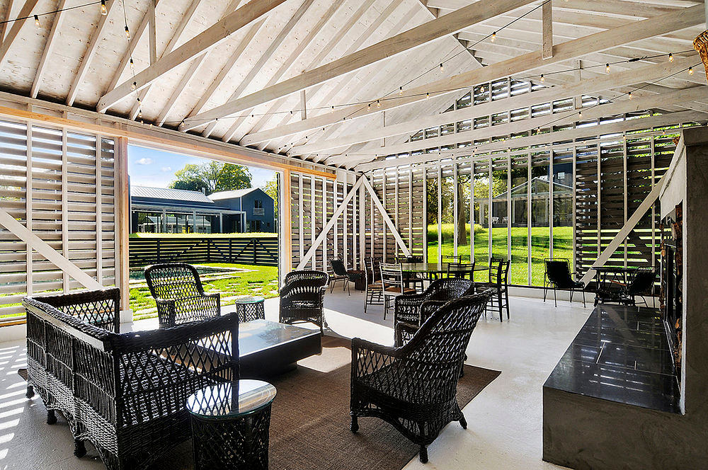 Wooden beamed ceiling, floor-to-ceiling windows, rattan furniture, and a lush outdoor view.