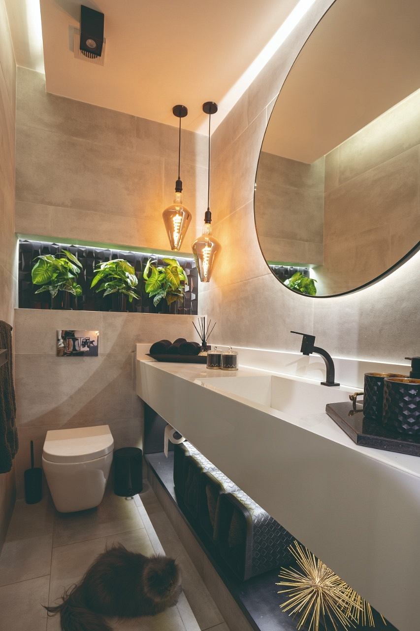 Warm-toned bathroom with round mirrors, pendant lights, and greenery accents. Sleek vanity with black fixtures.