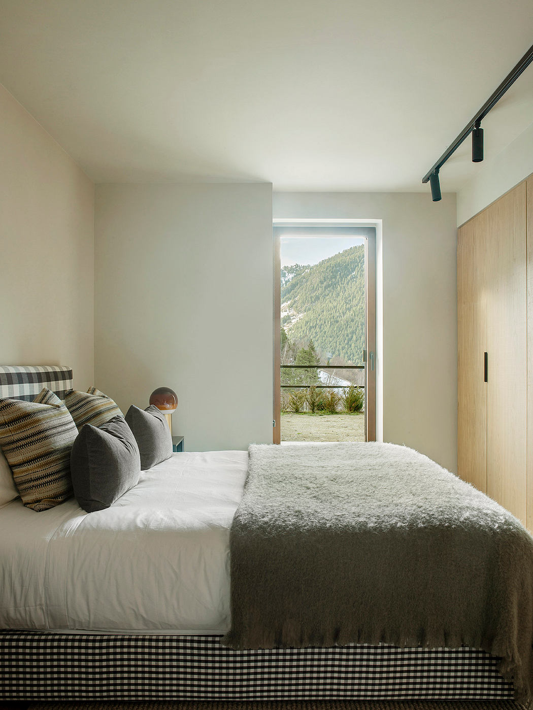 Cozy bedroom with a large window overlooking forested mountains, featuring a plush bedding and modern decor.