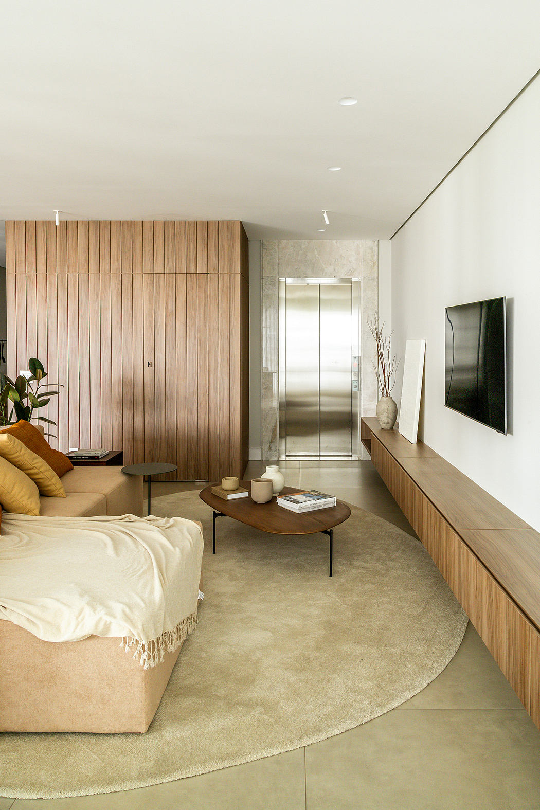 Minimalist living room with warm wood paneled walls, plush beige sofa, and modern decor.